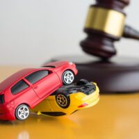 Car accident, auto insurance and judge gavel law concept. Red and yellow car model crash, wooden judge hammer on wooden table with white wall background copy space.